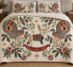 Two illustrated sunbitterns with striped heads, orange legs and spread eye-patched orange, black and cream wings frame one tan-and-ivory toy rocking fennec with a navy chest panel with oversized ears, an ivory face, navy saddle with ochre botanical detail and cranberry rocker, fig halves, cedar, holly, mistletoe and ochre stars on ivory with cranberry binding. Flat printed Christmas artwork. Includes one quilt and two matching pillow shams. Dense sewn quilting, shallow fill and natural fabric drape.