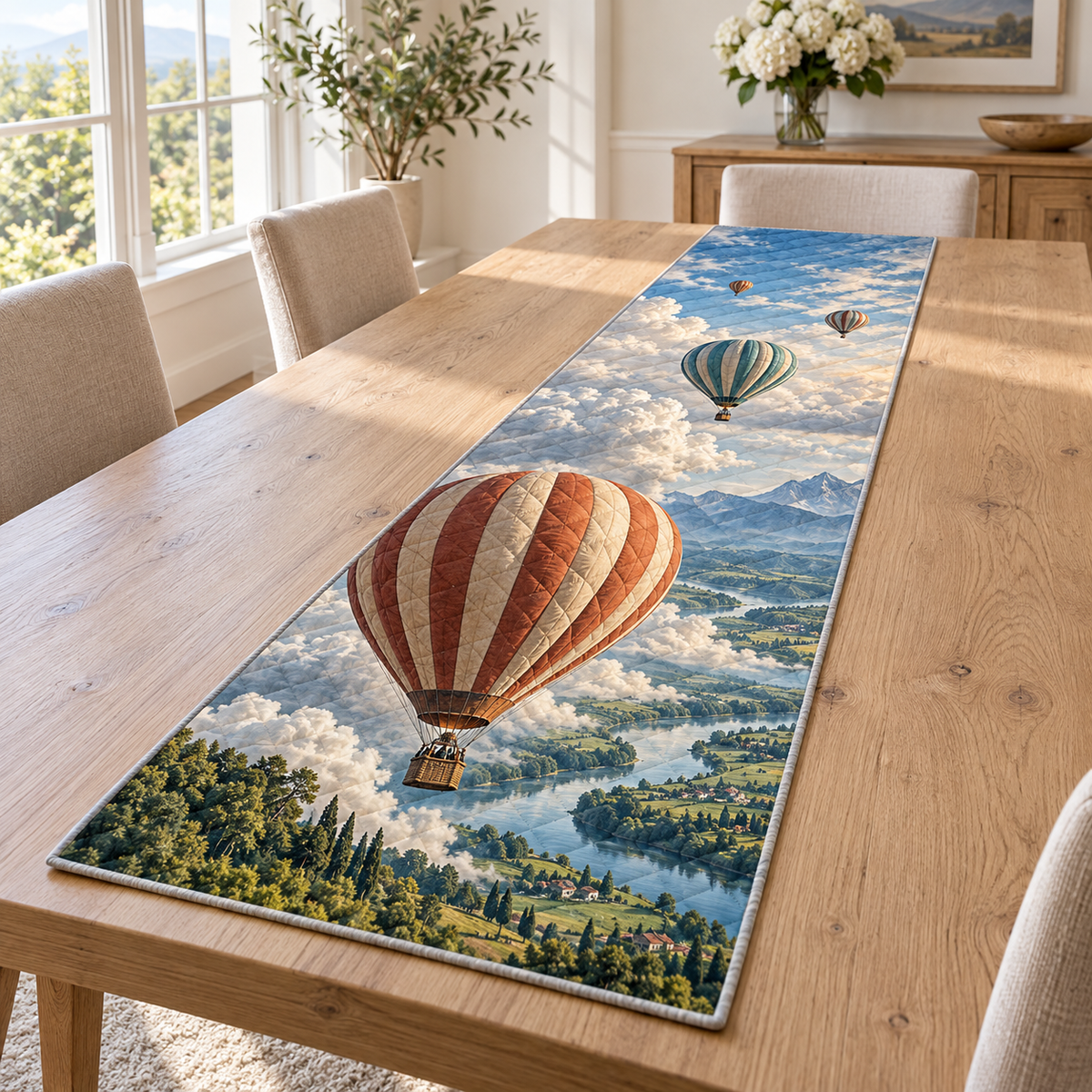 A rectangular table runner printed with layered hot air balloons, billowing clouds, a winding river and distant mountain fields.