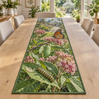 A rectangular table runner printed with butterfly eggs, a striped caterpillar, green chrysalis and orange butterfly in a layered garden.