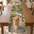 A rectangular table runner printed with a golden retriever carrying a rope ring across a garden pond bridge.