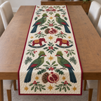 Four illustrated green turacos frame two cranberry toy rocking elephants with navy rockers and ochre saddles, with pomegranate halves, cedar cones, holly, mistletoe and ochre stars on ivory with cranberry binding. Flat printed Christmas artwork. Includes one table runner. Quilted cotton hero with visible sewn quilting and fabric drape.