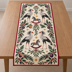 Four illustrated secretarybirds with black quill crests and long legs frame two navy toy rocking zebras with ochre saddles and cranberry rockers, plum halves, cedar, holly, mistletoe and ochre stars on ivory with cranberry binding. Flat printed Christmas artwork. Includes one table runner. Quilted cotton hero with visible sewn quilting and fabric drape.