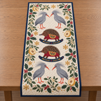 Four illustrated ash-gray kagus with swept-back crests and red-orange bills and legs frame two cranberry toy rocking echidnas with ochre saddles and navy rockers, quince halves, cedar, holly, mistletoe and ochre snowflakes on ivory with navy binding. Flat printed Christmas artwork. Includes one table runner. Quilted cotton hero with visible sewn quilting and bound fabric edges.