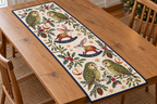 Four illustrated moss-green kakapo parrots with pale facial discs frame two cranberry toy rocking bilbies with long pink-lined ears, pointed snouts, ochre saddles and navy rockers, red apple halves, cedar, holly, mistletoe and ochre snowflakes on ivory with navy binding. Flat printed Christmas artwork. Includes one rectangular table runner. Dense sewn quilting, shallow fill and flat lay on an oak table.