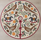 Four illustrated great argus pheasants with speckled brown plumage, blue heads, long tails and cream eye-spotted wing feathers frame two navy toy rocking coatis with pointed snouts, ringed tails, ochre saddles and cranberry rockers, orange halves, cedar, holly, mistletoe and ochre stars on ivory with cranberry binding. Flat printed Christmas artwork. Includes one circular tree skirt with center opening and tie closure. Visible sewn quilting and continuous radial opening.